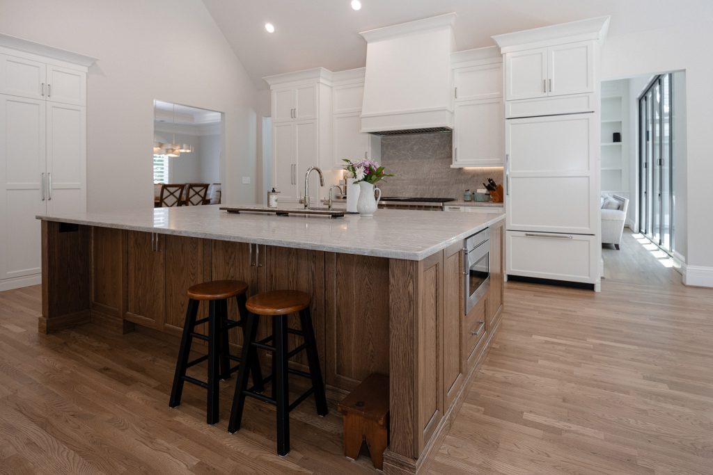 Stained-oak kitchen island with quartz counters and black-and-wood barstools under a vaulted ceiling.