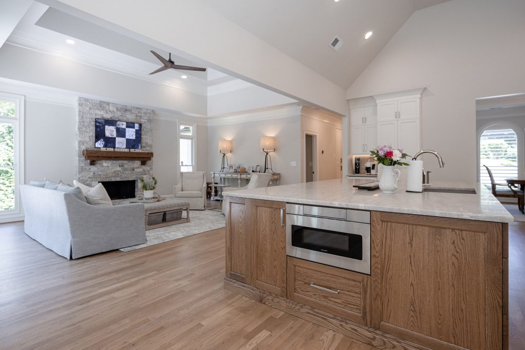 Open-concept kitchen and living room with an oak island, microwave drawer, and a stacked-stone fireplace beyond.