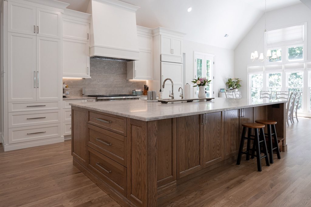 Spacious kitchen with white cabinetry, a large oak island, black barstools, and white oak floors.