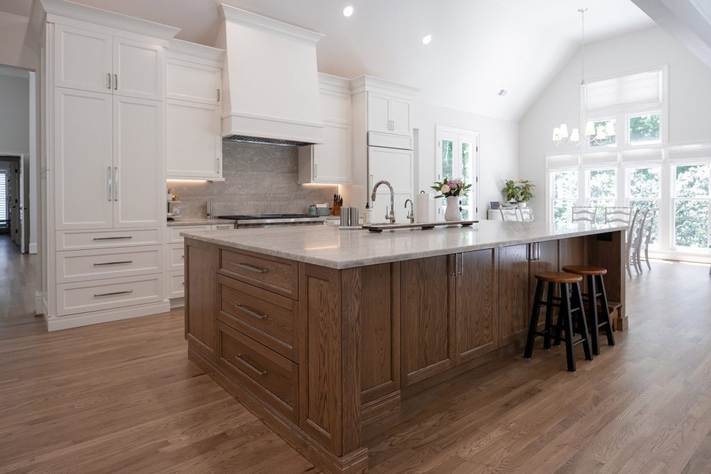 Open kitchen with white cabinets, a stained-oak island, quartz counters, and a vaulted ceiling over a breakfast area.