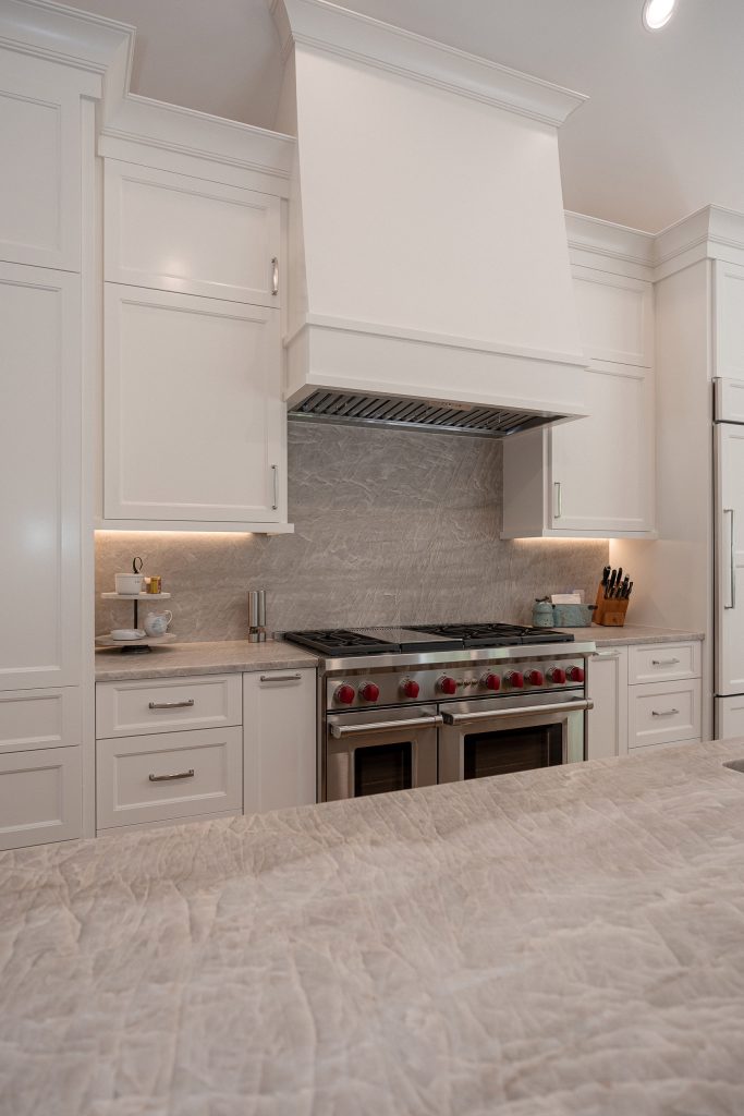 White kitchen range wall with a Wolf range and painted hood beyond a soft-veined quartz island counter.