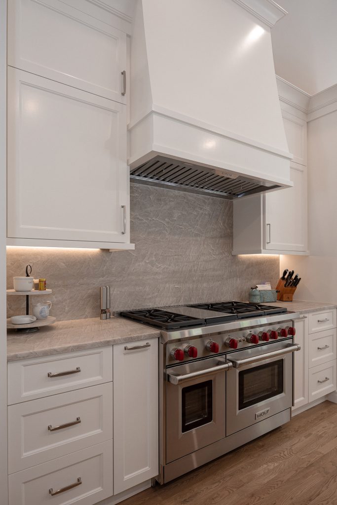 White range wall with a custom painted hood, a stainless Wolf range, and a veined stone-slab backsplash.