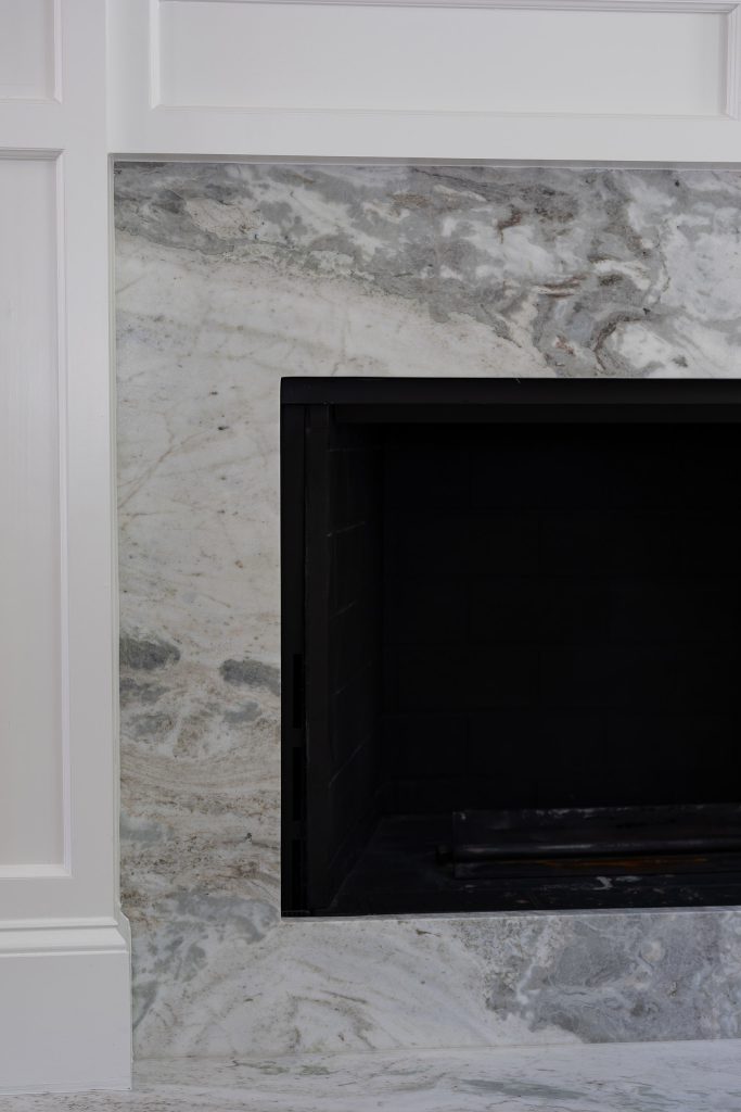 Detail of a white paneled fireplace with a grey-and-tan veined quartzite slab surround and black firebox.