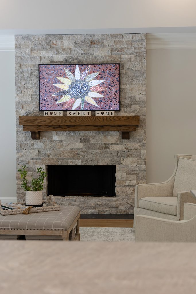 Living room fireplace in silver travertine ledgestone with a terrazzo sunflower artwork above the oak mantel.
