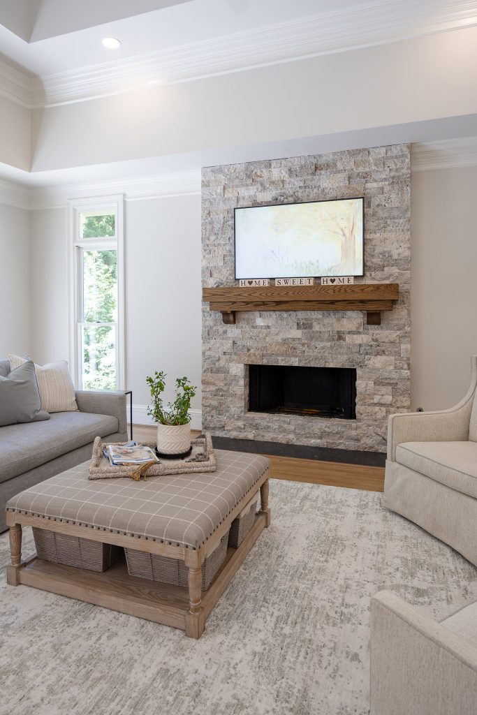 Family room with a stacked-stone fireplace, wood mantel, gray sofa, and cream swivel chairs on a soft rug.