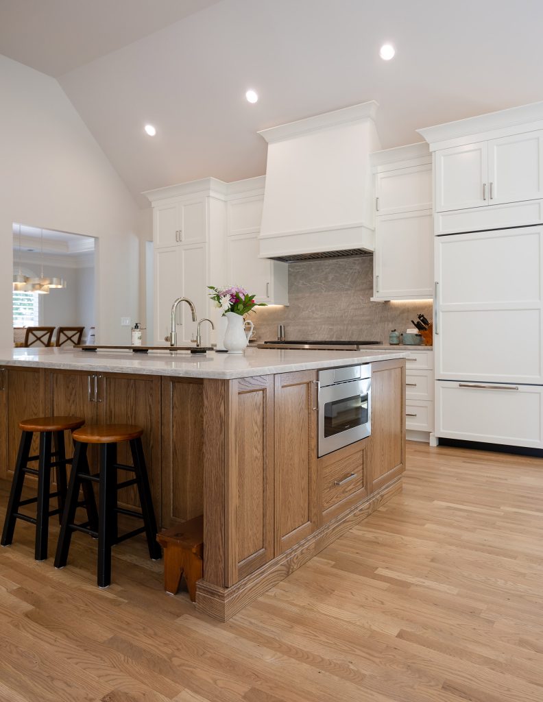 Custom kitchen with white paint-grade cabinetry, a stained white oak island, quartzite countertop and slab backsplash, and refinished oak floors.