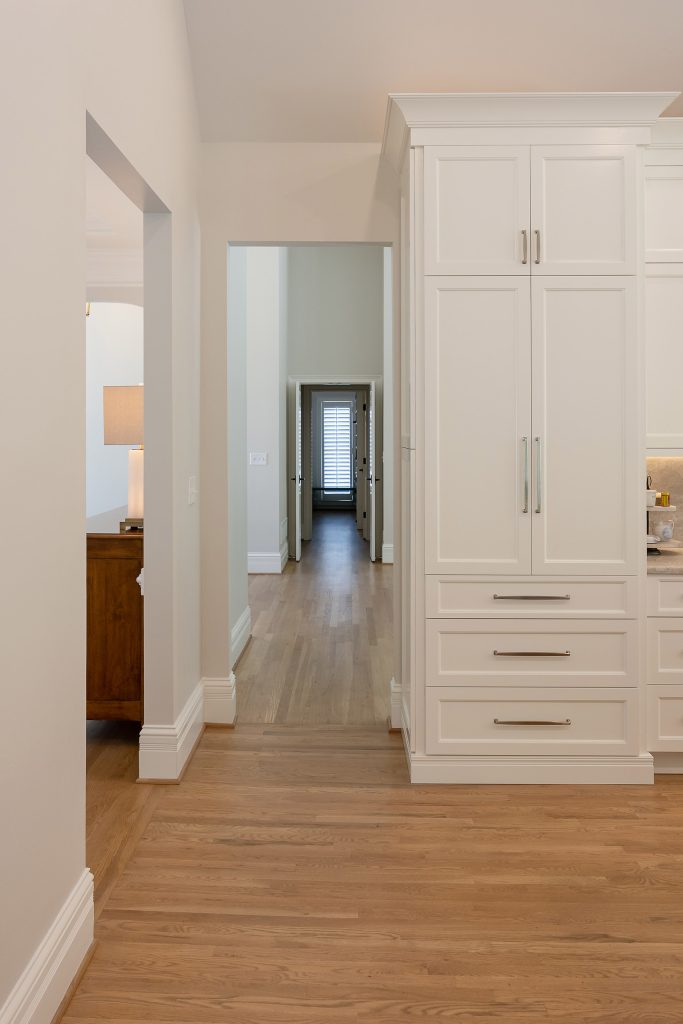Hallway with a floor-to-ceiling white pantry cabinet, brushed-nickel bar pulls, and white oak flooring.