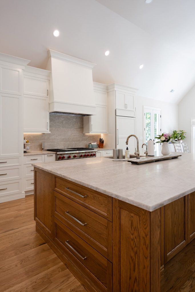 Vaulted kitchen with white perimeter cabinets, a stained-oak island, quartz counters, and a stainless Wolf range.