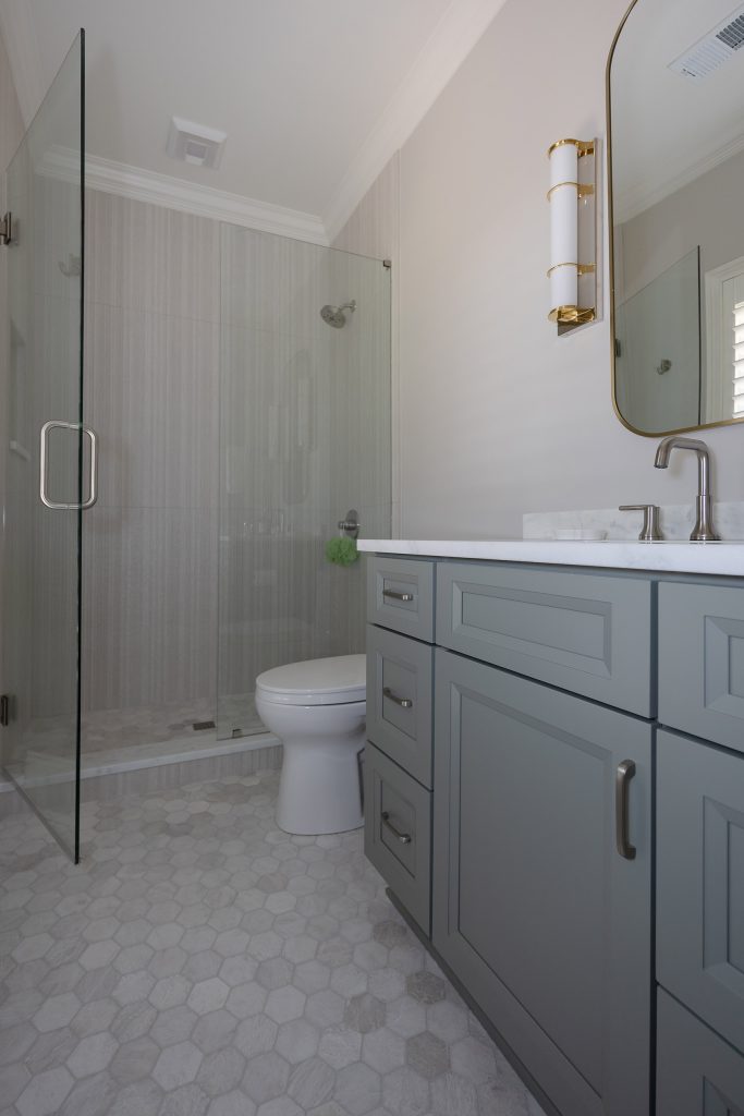 Guest bathroom with a frameless glass shower, grey shaker vanity, marble-look counter, and hexagon tile floor.