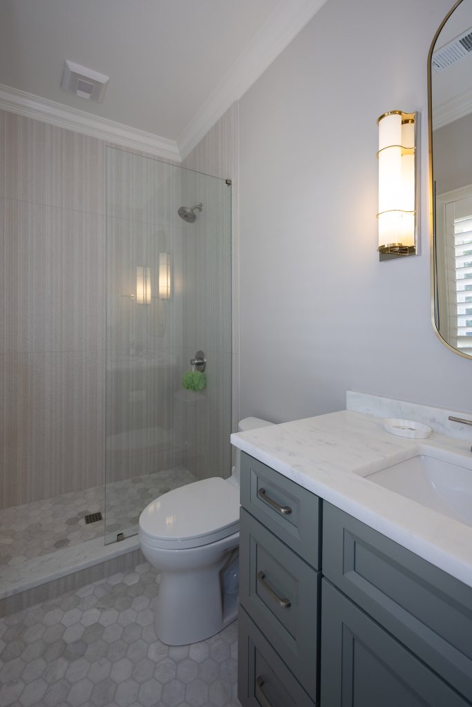 Guest bath with a glass shower in vertical linen-look tile, a grey vanity, and a marble hex floor.