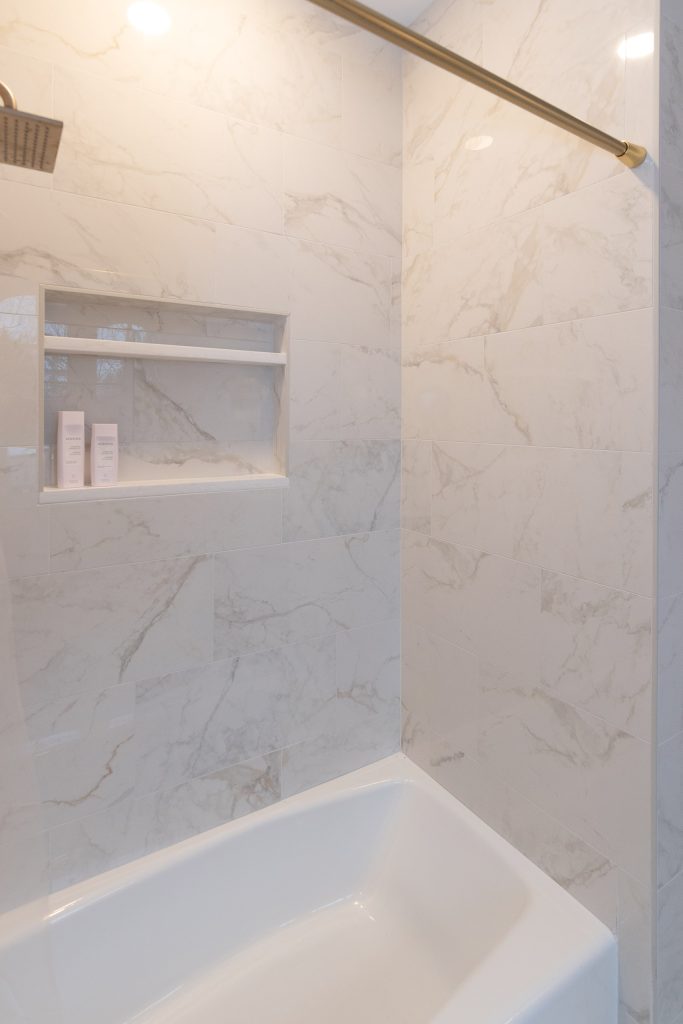 Tub-shower surround in white and gray marble-look tile with a brushed-gold curtain rod and a recessed niche.
