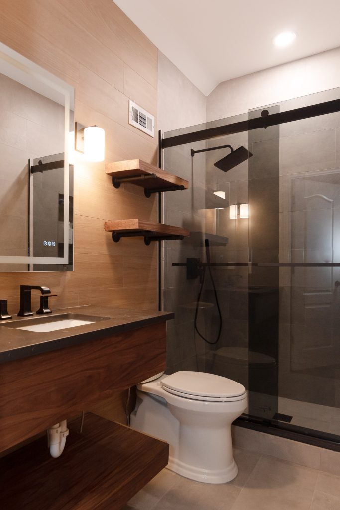 Contemporary bathroom with wood-look tile, a dark quartz vanity top, floating walnut shelves, and a black-framed glass shower.