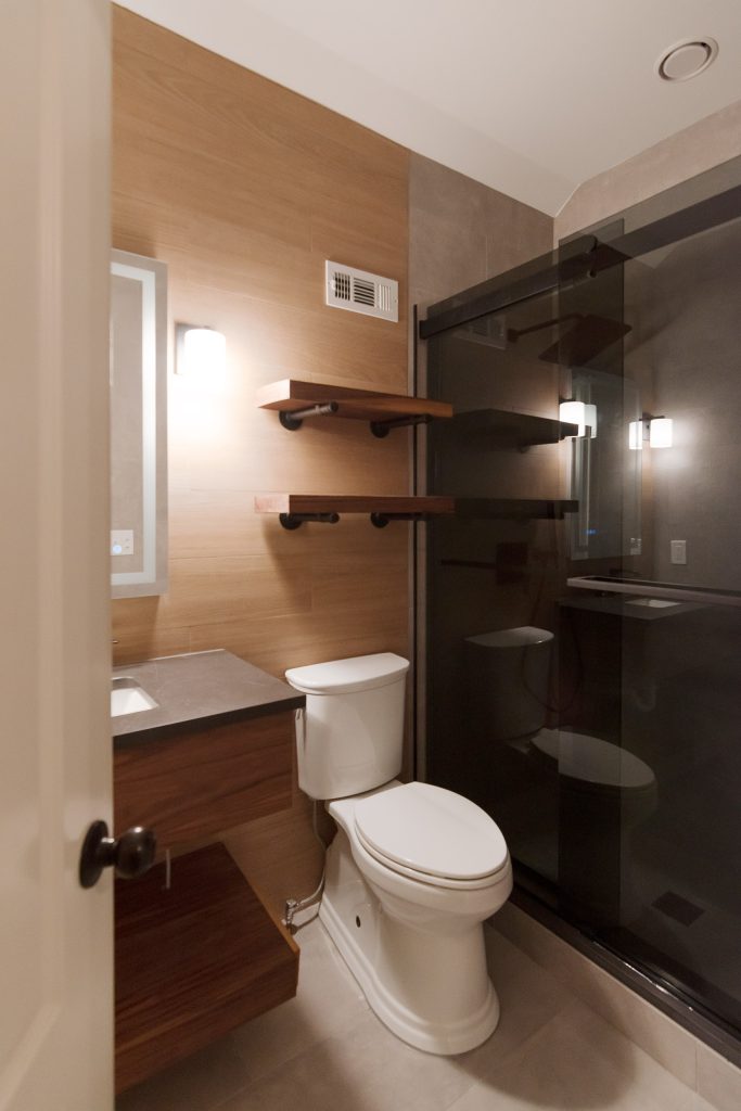Compact modern bath with a floating walnut vanity, wood-look tile, live-edge shelves, and a dark-glass shower.