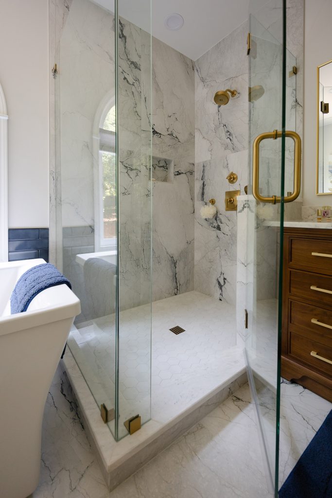 Marble-look shower with white hexagon mosaic floor, gold square drain, and gold fixtures beside the freestanding tub.