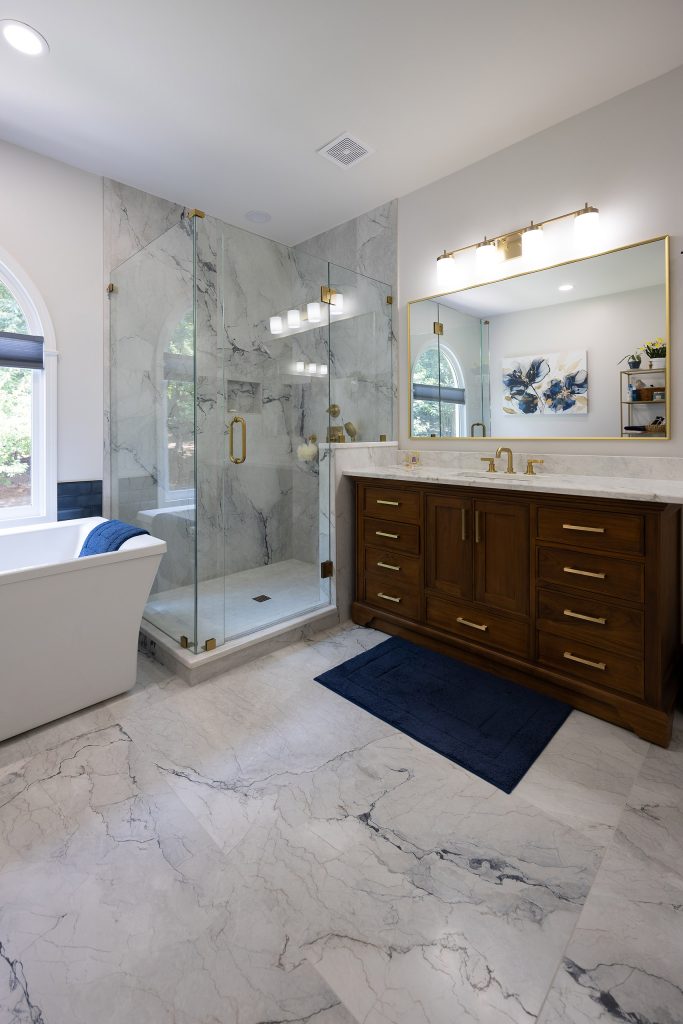 Master bath with a freestanding tub, corner glass shower in marble-look tile, walnut vanity, and marble-look floors.