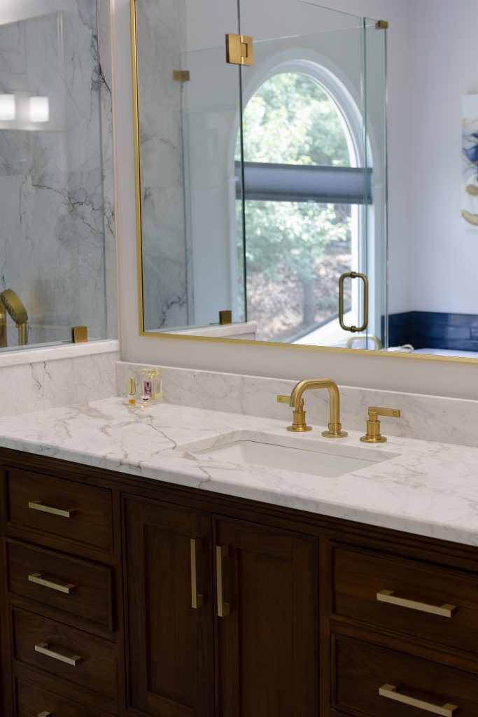Walnut vanity with white quartz counter, gold widespread faucet, and a gold-framed mirror over an undermount sink.