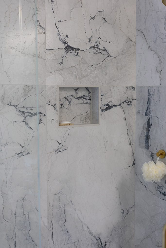 Large-format marble-look shower tile with bold blue-gray veining and a recessed niche holding a bar of soap.