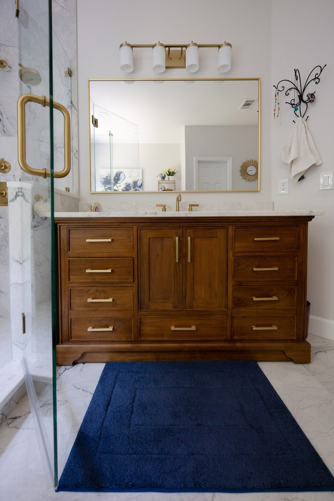 Walnut vanity with brushed-gold pulls, white quartz counter, gold-framed mirror, and a navy runner rug.