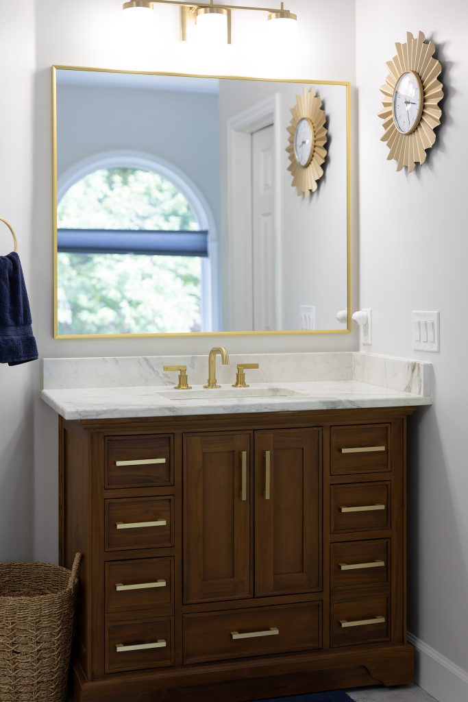 Second walnut vanity with brushed-gold pulls, white quartz top, gold-framed mirror, and a gold sunburst clock.