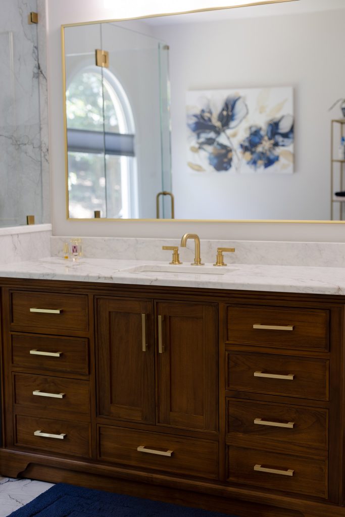 Walnut vanity with brushed-gold bar pulls, white quartz counter, undermount sink, and a gold-framed mirror.