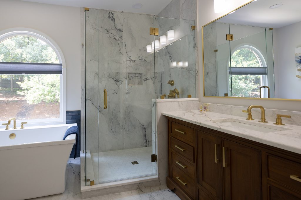 Master bath from an angle with freestanding tub, glass shower in marble-look tile, and walnut vanity.