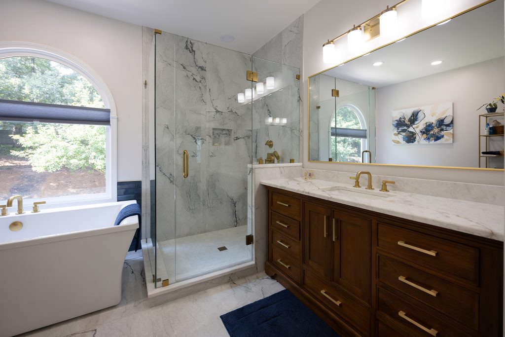 Transitional master bath with freestanding tub, marble-look corner shower, and walnut vanity with gold hardware.