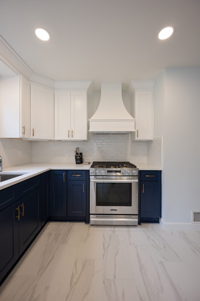 Stainless gas range flanked by navy base cabinets and white uppers, with a custom white hood and glazed subway-tile backsplash.