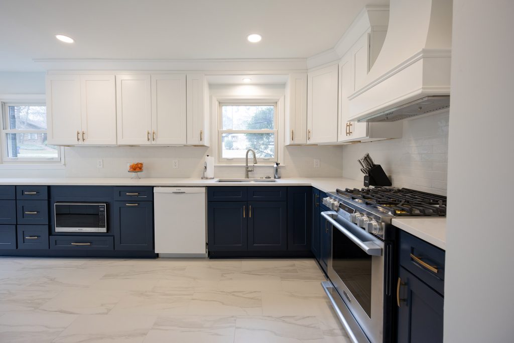 Two-tone kitchen with navy base cabinets, white uppers, brushed-gold hardware, white quartz counters, and a stainless gas range.
