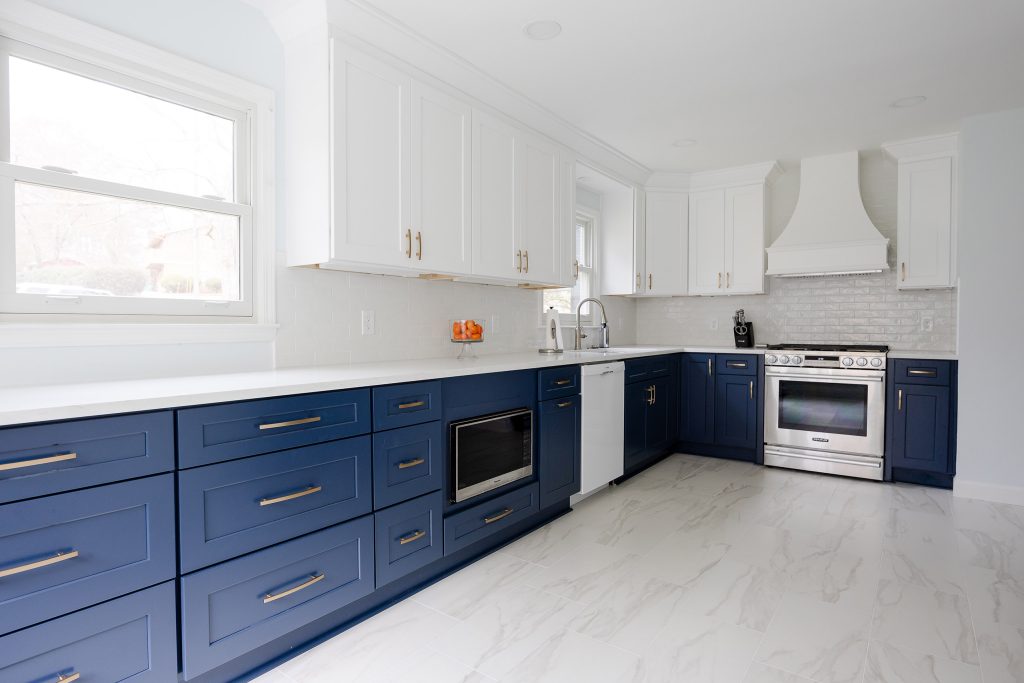 Two-tone kitchen with navy drawers below a window, white uppers, a built-in microwave, and a stainless range at right.