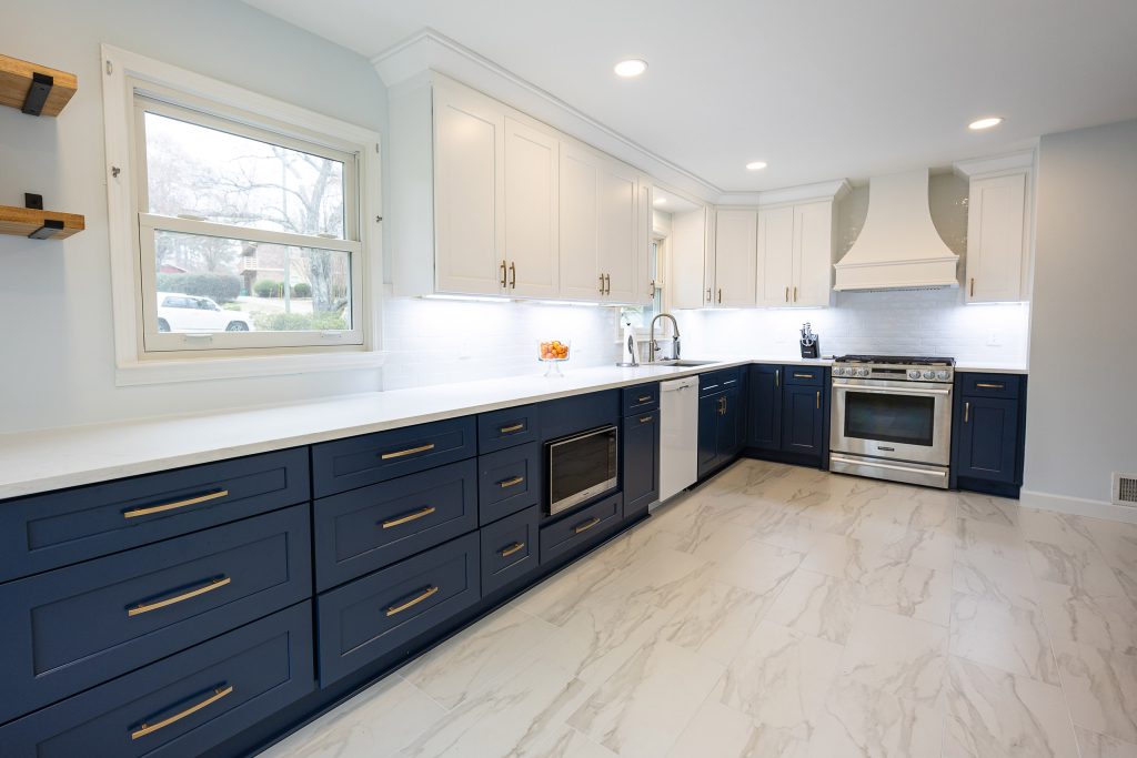 Kitchen with floating wood shelves, a window, navy shaker drawers, white uppers, and a stainless range under a white hood.
