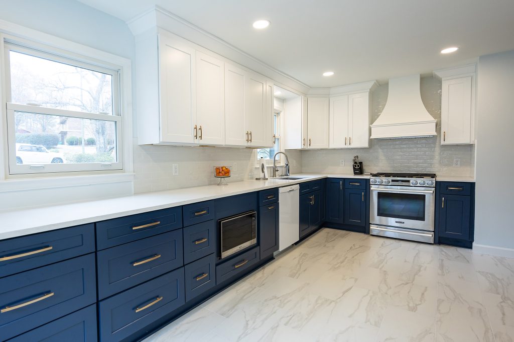 Two-tone kitchen with a window over navy drawers, white uppers, white quartz counters, and a custom white hood at the corner.