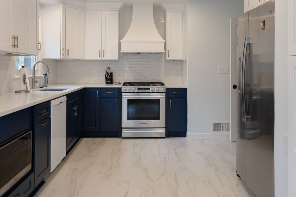 Stainless gas range under a custom white hood, flanked by navy base cabinets and white uppers with brushed-gold hardware.