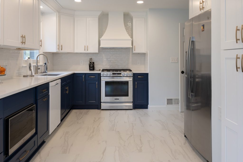 Galley view of a two-tone kitchen with white uppers, navy lowers, a custom white hood, and stainless appliances.