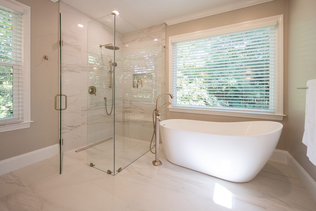 Freestanding soaking tub beside a frameless glass walk-in shower with marble-look tile and brushed-gold fixtures.