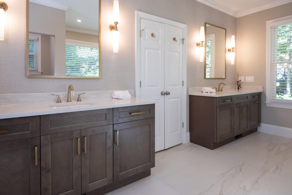 Double-vanity master bath with gray-brown shaker cabinets, white quartz counters, and brushed-gold fixtures.