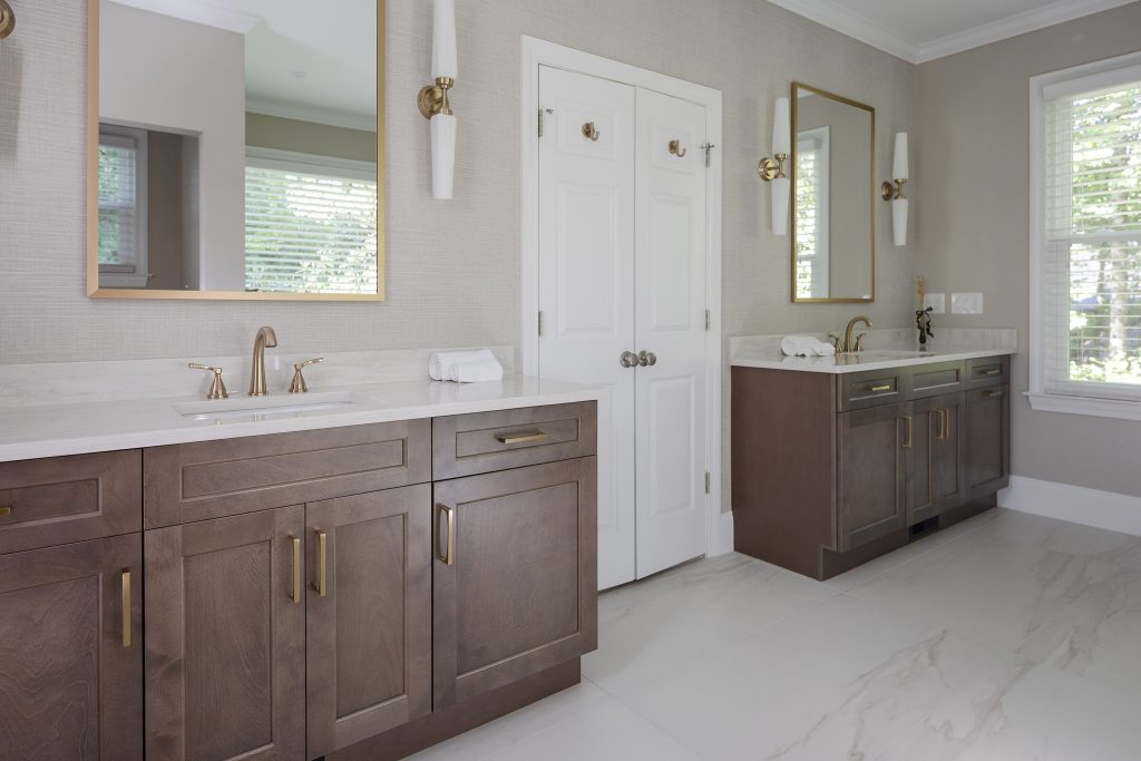 Two dark-stained vanities with white quartz tops and brushed-gold fixtures flanking a white closet door.