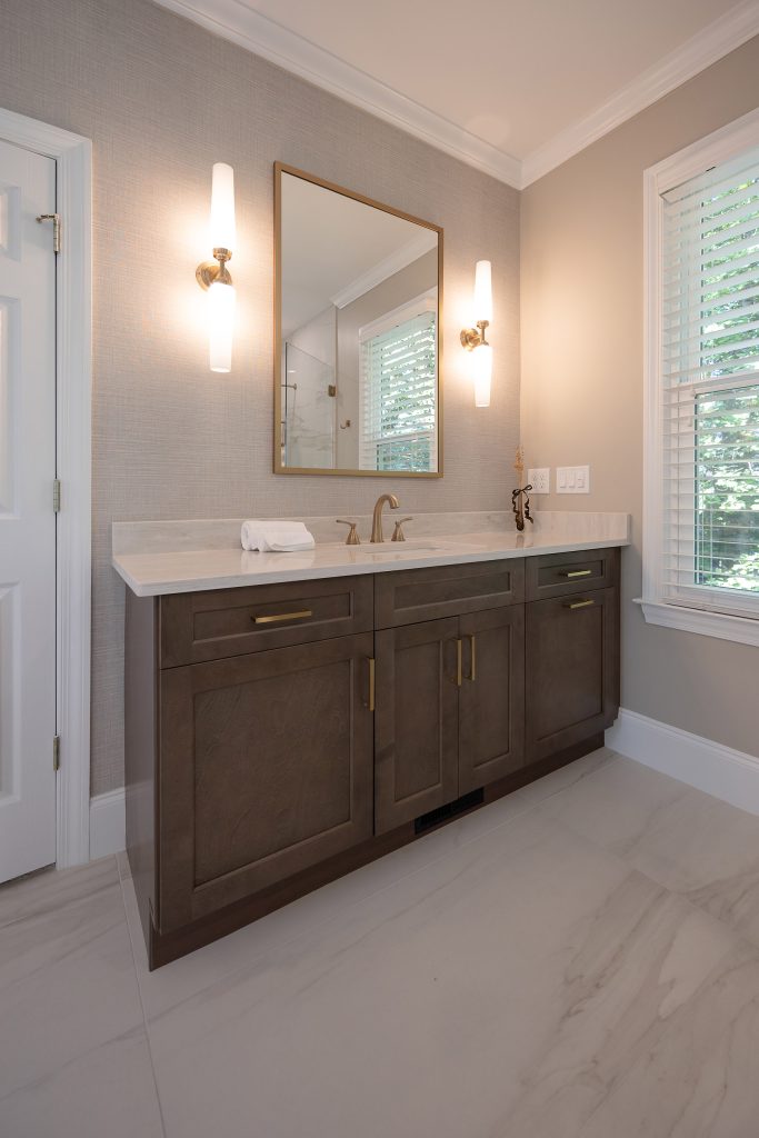 Dark shaker vanity with cream quartz counter, brushed-gold faucet and pulls, gold-framed mirror, and white-glass sconces.