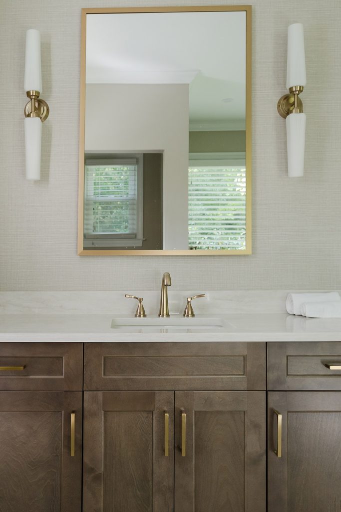 Dark shaker vanity with white quartz top, brushed-gold faucet and pulls, gold-framed mirror, and white-glass sconces.