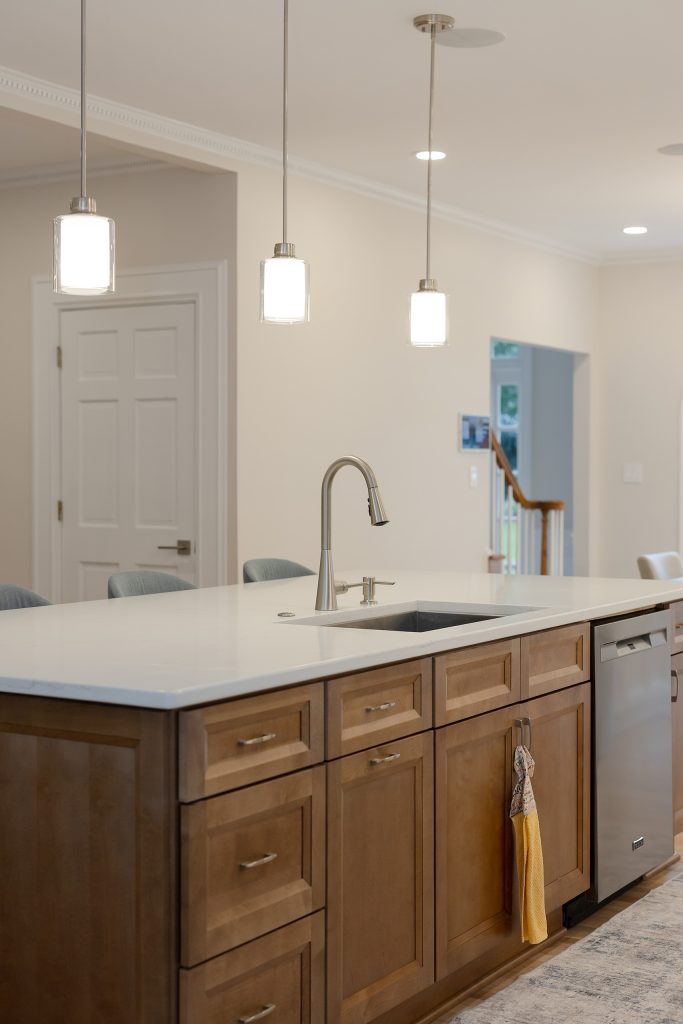 Island detail with an undermount sink, pull-down faucet and integrated dishwasher set into stained maple cabinetry beneath quartz.