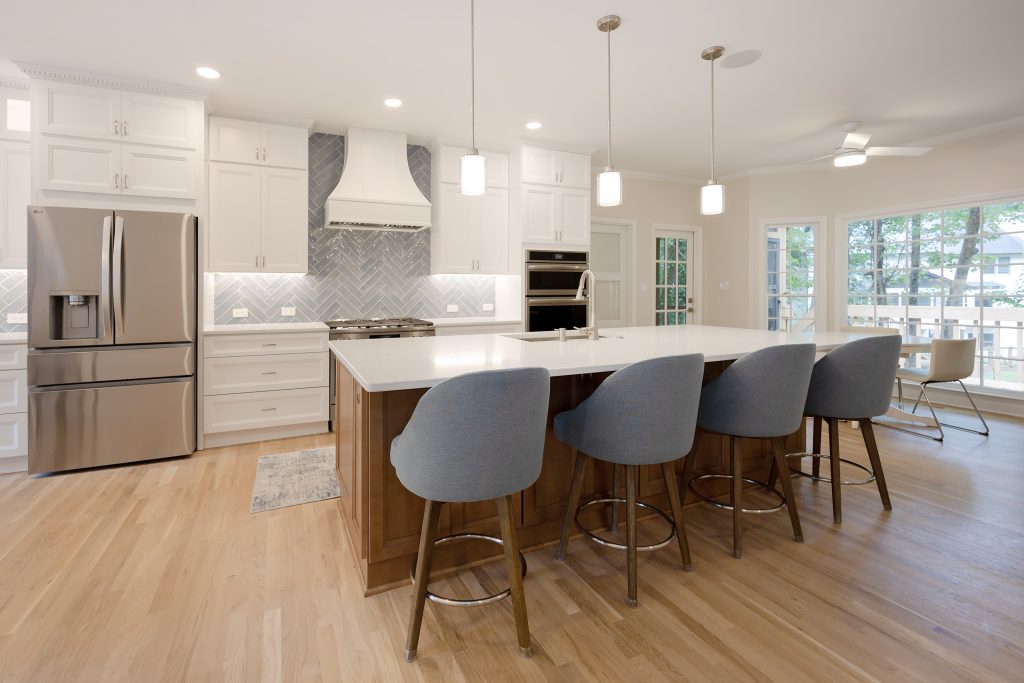 Wide kitchen view toward the family room, with the island, counter stools and windows beyond the open plan.