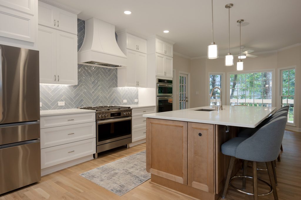 Open kitchen with refrigerator, range and island in one sightline, and French doors to the screened porch on the right.