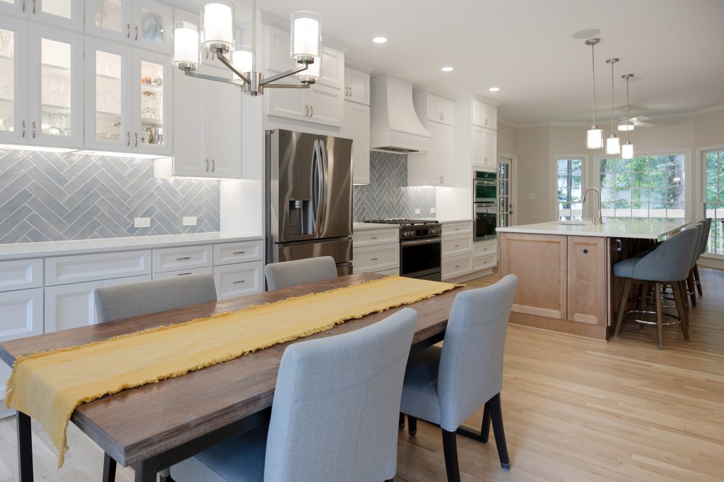 Dining table beneath a linear chandelier, with the bar cabinetry to the left and the kitchen island beyond.