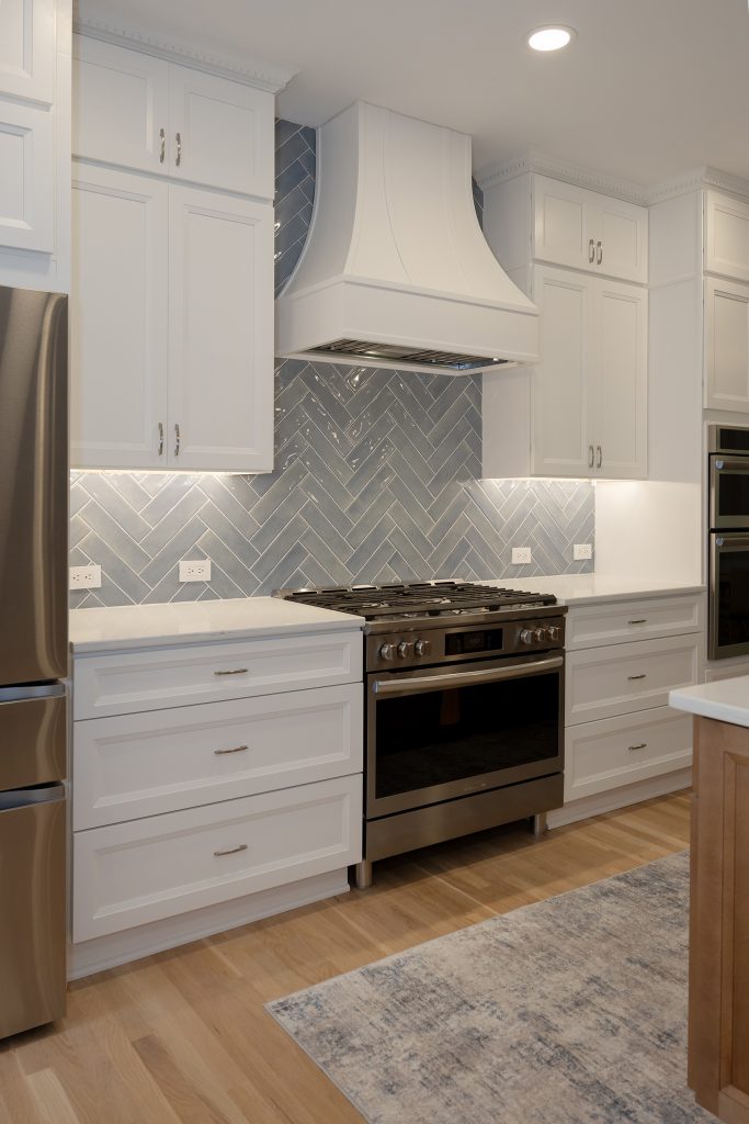 Range wall with curved white hood and herringbone tile, framed by the refrigerator and a runner rug on white oak flooring.