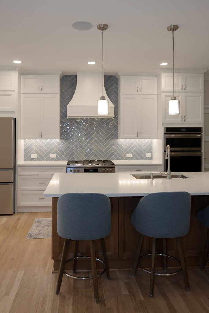 Quartz island with counter stools in the foreground and the range, hood and wall ovens behind.