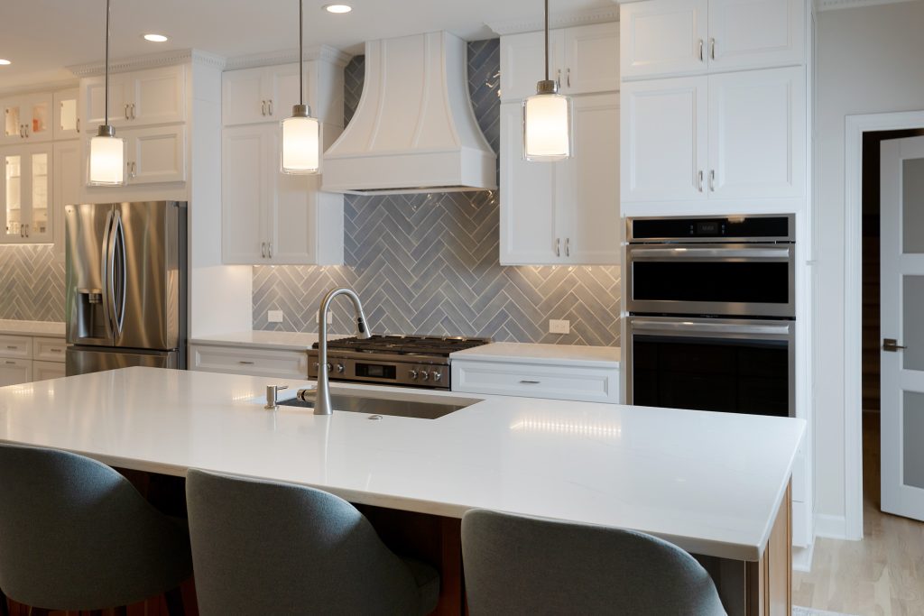 Island sink and faucet in the foreground with the range, hood and double wall ovens beyond.