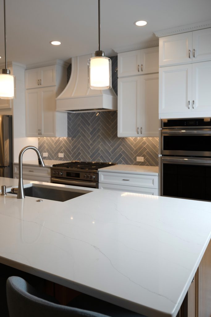 Close view of the veined quartz island countertop with the herringbone backsplash and range behind.
