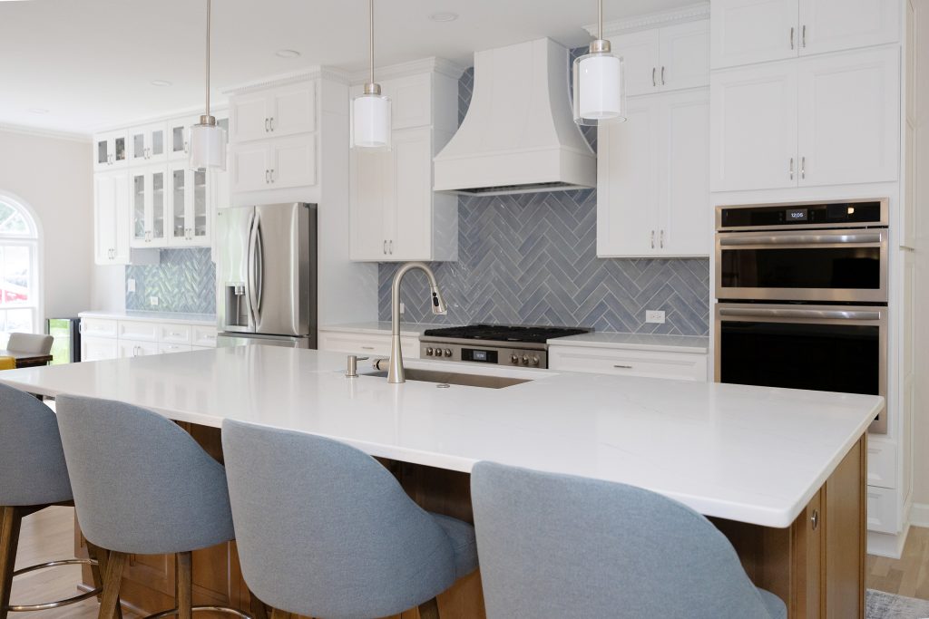 Kitchen with glass-front bar cabinetry at left, refrigerator, custom hood and a four-seat island.