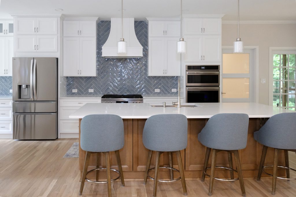 Open kitchen with a stained maple island, four blue counter stools and French doors to the screened porch.