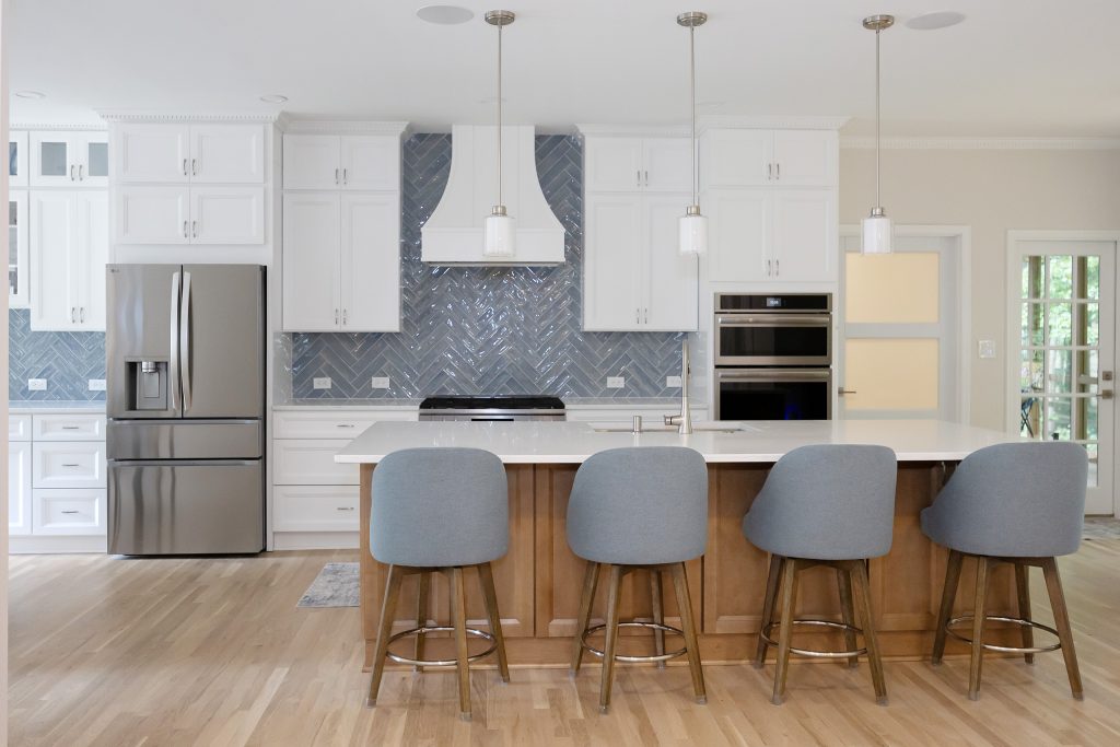 View across the dining chairs to the island and kitchen, showing the continuous white oak floor.