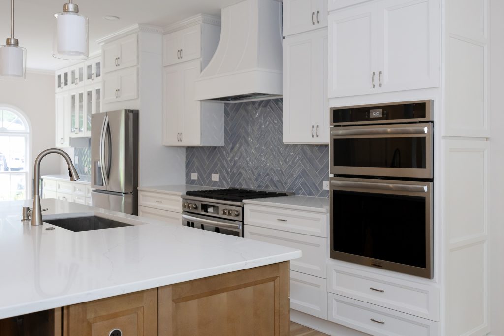 Island sink in the foreground with the range, custom hood and stacked wall ovens beyond.